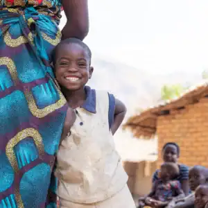 Child standing beside an adult in a village community.