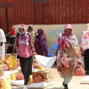 People carrying bags of emergency food for a month and supplies in an outdoor market area.