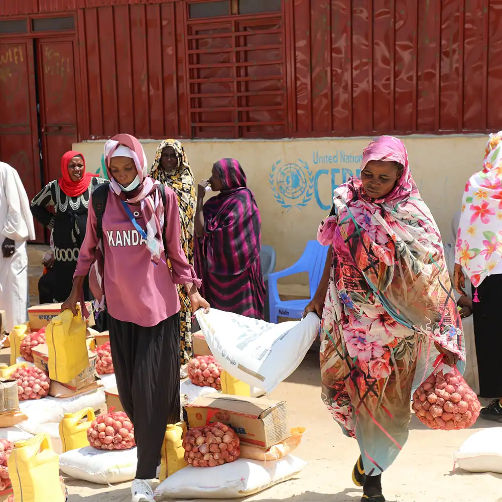 People carrying bags of emergency food for a month and supplies in an outdoor market area.