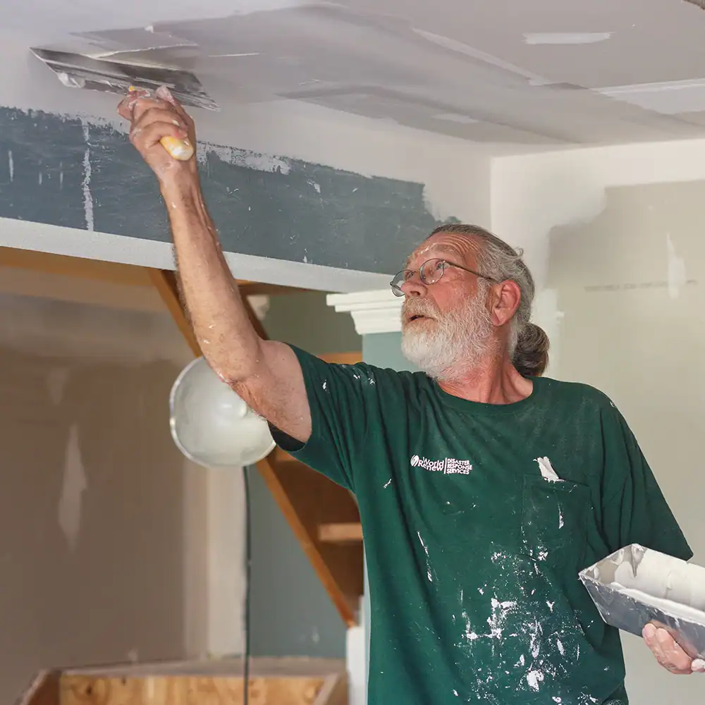 Volunteer using a drywall tool during a home repair project.